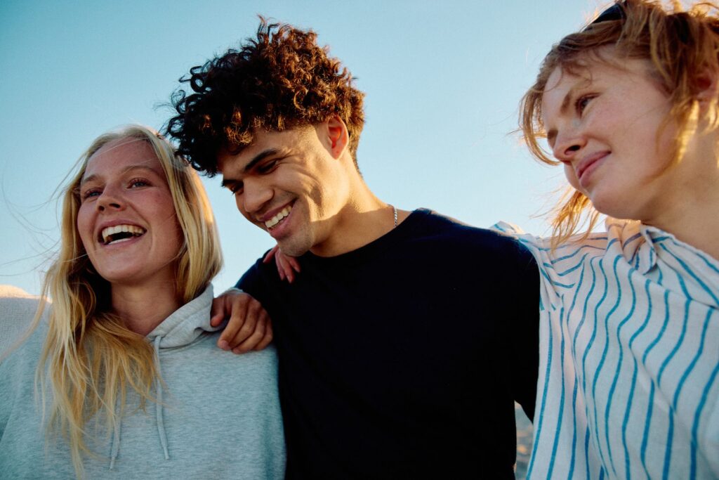 Three confident teenagers laughing together outdoors in warm evening light