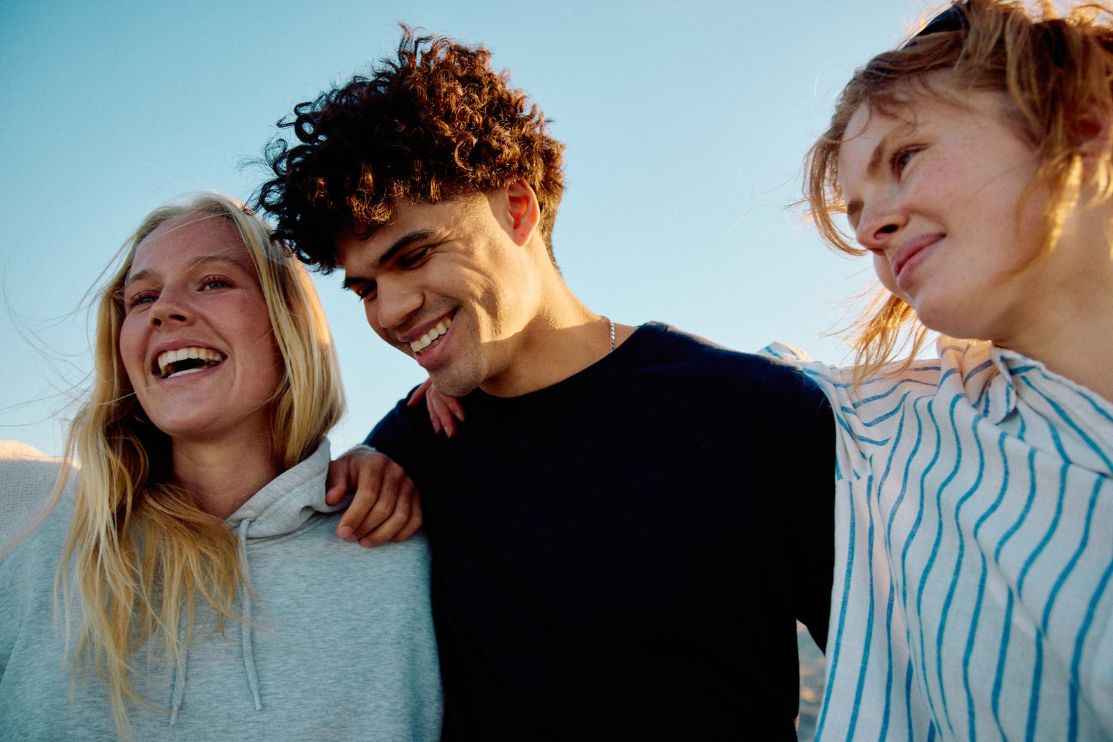 Three confident teenagers laughing together outdoors in warm evening light