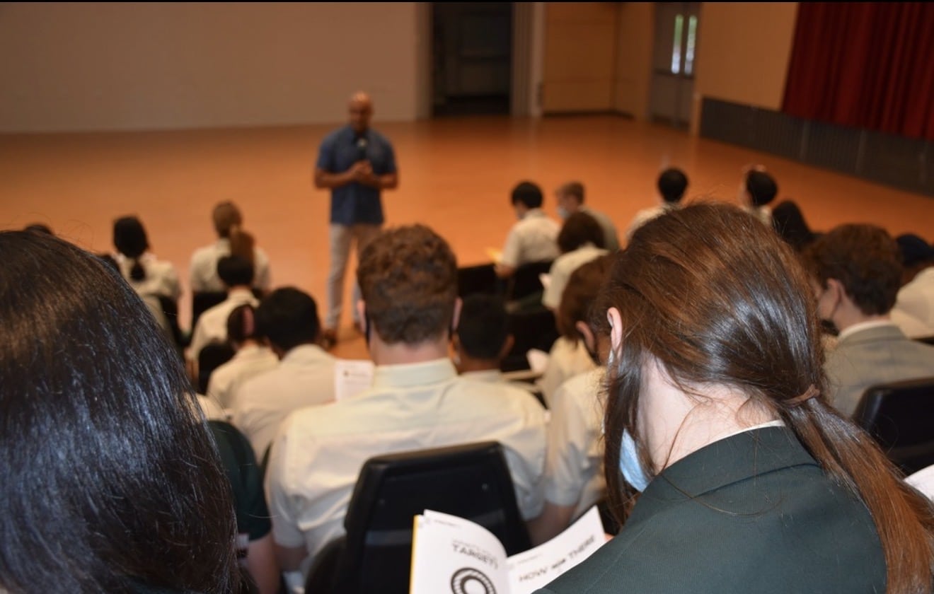 Secondary students in uniform listening to a guest speaker at a school seminar