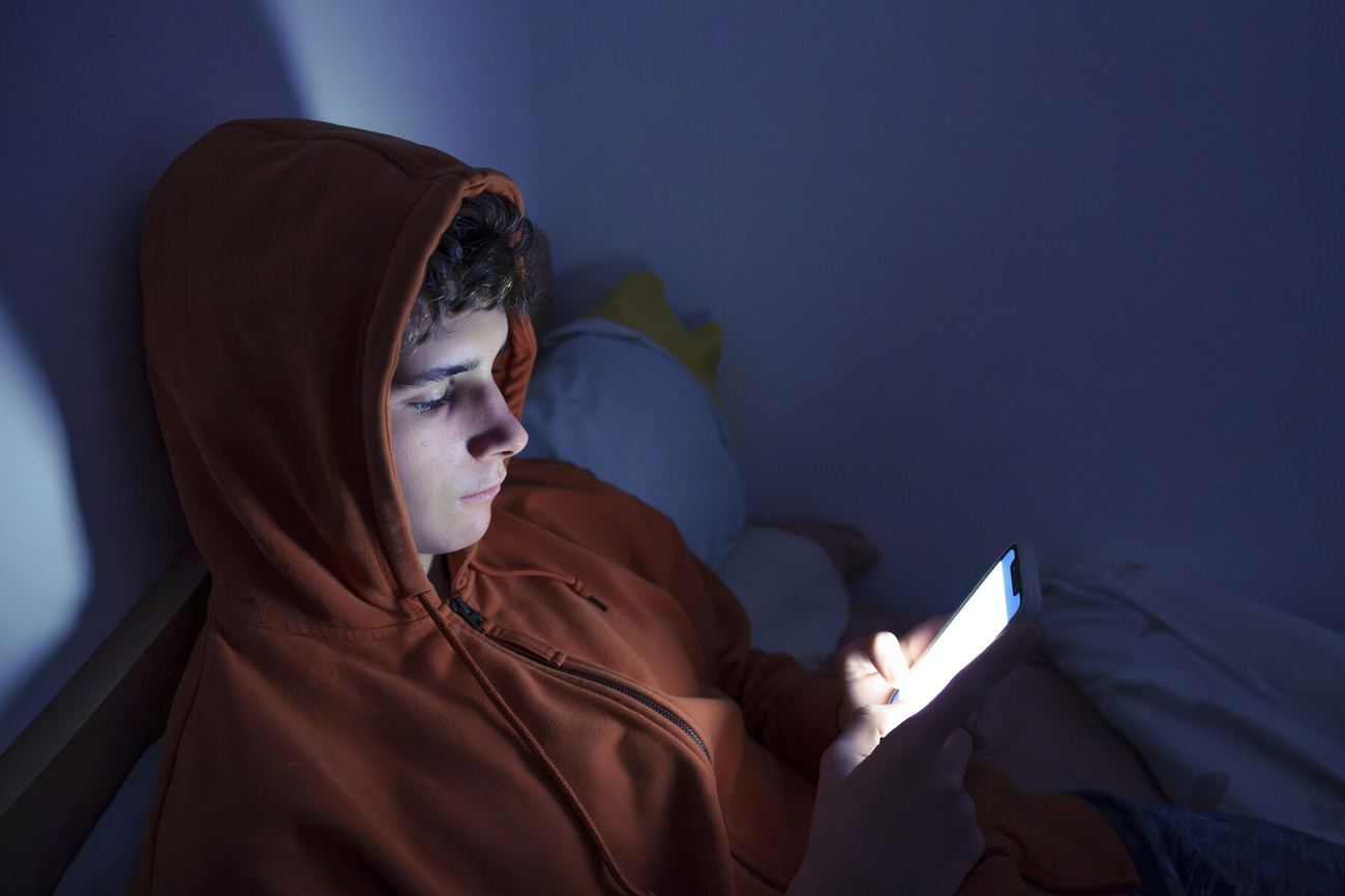 A teenage boy lit by his phone screen, late at night